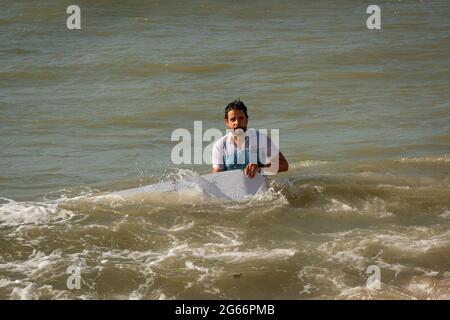 Uribia, la Guajira, Colombia - Maggio 27 2021: Giovane uomo Latino bagnato sta portando una Surfboard dopo aver scivolato sulle dune di Taroa e cadendo nel Mare W. Foto Stock