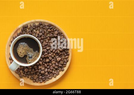 Vista ad alto angolo del caffè e dei chicchi di caffè posizionati in un vassoio di legno rotondo lo sfondo è giallo brillante corrugato motivo, spazio di copia. Foto Stock