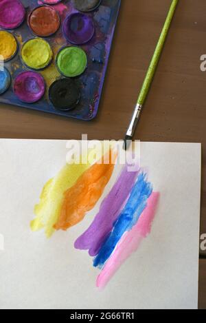 Un pezzo di carta bianca con colori dipinti di un bambino accanto a una scatola di vernice con vernici ad acquerello e un pennello Foto Stock