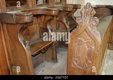 Aquila a testa doppia e teste di legno intagliate sulla stalla del coro risalente al 16 ° secolo a St Beunos, Clynnog Fawr, Galles Foto Stock