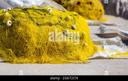 Le reti da pesca si accatastano sul molo del porto di fisher che si asciugano sotto il sole. Reti da pesca di colore giallo con corde e galleggianti. Isola greca Cicladi attrezzatura di pescatori Foto Stock