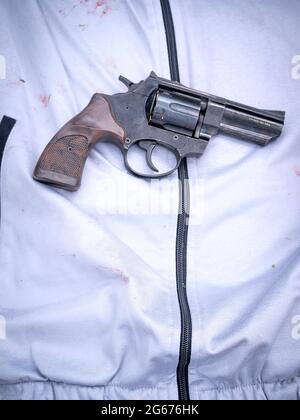 Vista verticale del revolver 9mm posto sulla tuta bianca del maschio. Foto Stock
