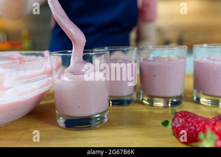 il processo di preparazione di un dessert alla fragola dal latte. Cuoco mette il pudding in tazze e decora Foto Stock