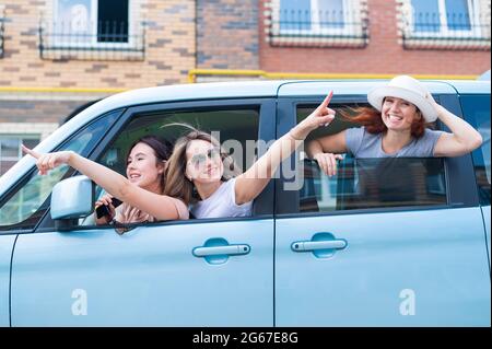 Tre allegre girlfriends caucasiche si affacciano dalla finestra dell'auto. Le donne eccitate vanno in viaggio. La bionda di brunette e la testa rossa stanno andando avanti Foto Stock