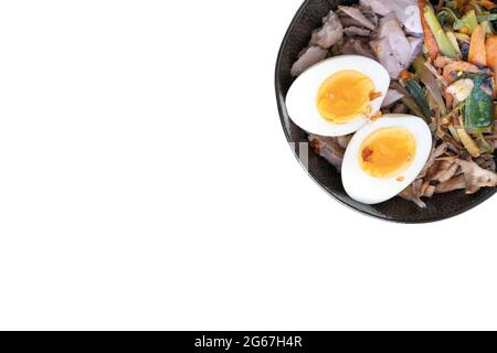 Studio di ciotola nera di tagliatelle di ramen con uova bollite, verdure e tacchino si incontrano, pronti per essere versati con brodo bollente isolato su bianco Foto Stock