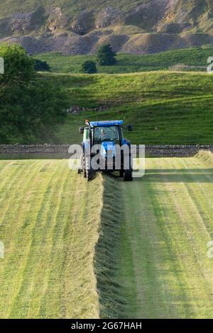 L'agricoltore che fa grandi balle rotonde di grandine con un trattore New Holland TS135 e una pressa McHale F5500, estata sera a Wensleydale, North Yorkshire Foto Stock