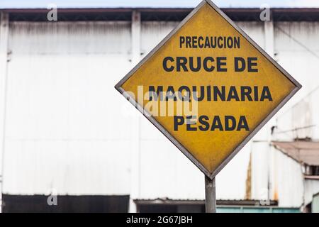 Cartello giallo con la scritta ´Precaucion Cruce de Maquinaria Pesada' (avvertimento incrocio di piante pesanti) in spagnolo Foto Stock