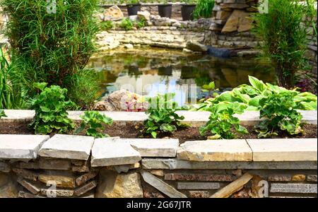 Progettazione paesaggistica di giardino casa piacevole, paesaggistica con pareti di ritegno, laghetto e aiuole in cortile casa residenziale. Splendido paesaggio outdo Foto Stock