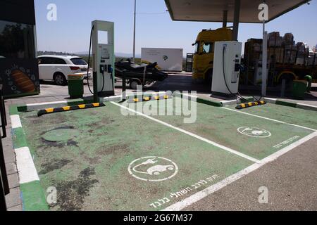 Due postazioni di ricarica per auto elettriche con posti auto verdi designati contrassegnati in ebraico solo per auto elettriche presso una stazione di benzina o un distributore di benzina. Foto Stock