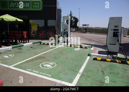 Due postazioni di ricarica per auto elettriche con posti auto verdi designati contrassegnati in ebraico solo per auto elettriche presso una stazione di benzina o un distributore di benzina. Foto Stock