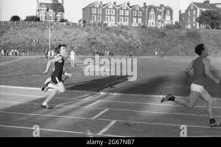 1960s, storico, atletico, fuori su una pista di cenere, tre giovani uomini che competono in una corsa ad una giornata di sport inter-contea, Inghilterra, Regno Unito. Foto Stock