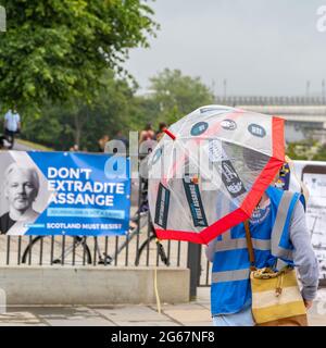 The Mound, Edinburgh, Scotland, UK, 3 luglio 2021: Un sostenitore di Julian Assange prende la copertura dalla pioggia sotto il suo ombrello, decorato con adesivi Assange. I sostenitori di Julian Assange scesero per le strade di Edimburgo per celebrare il 50° compleanno di Julian, una delle tante celebrazioni che si svolgono oggi in tutto il mondo. Julian Assange è ancora detenuto nella prigione di Belmarsh, mentre il governo degli Stati Uniti sta cercando di estradarlo in America, per le pubblicazioni di informazioni trapelate sul suo sito web wikileaks. (Credit: Barry Nixon/Alamy Live News) Foto Stock