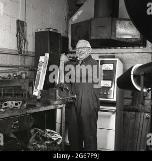 1970s, storico, all'interno di un'officina di riparazione di automobili, su un banco di lavoro con una morsa, un meccanico di officina anziano in tute che lavorano su un ammortizzatore o ammortizzatore per la sospensione di un'automobile, Inghilterra, Regno Unito. Foto Stock