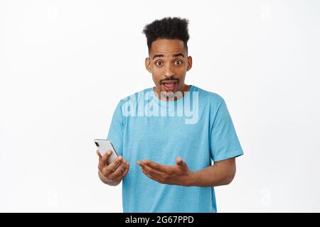 Entusiasta uomo afro-americano che tiene il telefono cellulare, entusiasta, guardando lo schermo, ricevere grandi notizie impressionante su social media app, sorpreso da Foto Stock