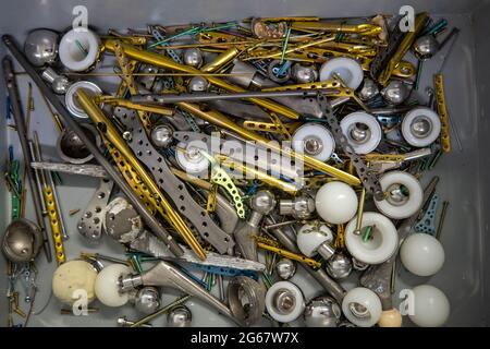 molte piastre in titanio espiantate, viti e protesi d'anca giacciono in una scatola di plastica grigia Foto Stock