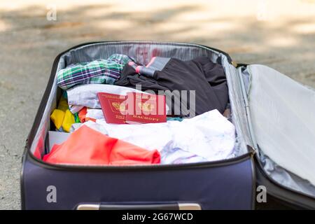 Una valigia aperta con le cose e due passaporti si trova sulla strada in una soleggiata giornata estiva. Messa a fuoco selettiva Foto Stock