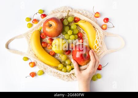 La donna mette la frutta matura in una borsa a maglia ecologica per lo shopping. Le mani femminili tengono un sacchetto di cotone con i prodotti biologici della fattoria. Stile di vita sostenibile Foto Stock