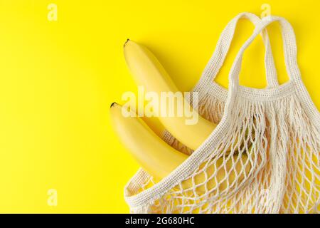 Banane mature in un sacchetto di maglia su sfondo giallo. Borsa in cotone ecologica. Frutta biologica. Stile di vita sostenibile e concep di rifiuti riciclabili Foto Stock