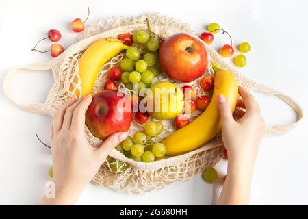 La donna mette la frutta matura in una borsa a maglia ecologica per lo shopping. Le mani femminili tengono un sacchetto di cotone con i prodotti biologici della fattoria. Stile di vita sostenibile Foto Stock