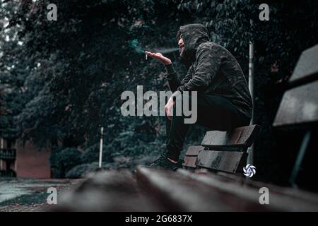 Uomo che fuma seduto sul divano nel giardino Lazy uomo che passa la giornata a fumare sigarette Foto Stock