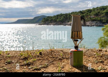 Caffè estratto in una piccola teiera su un bruciatore turistico vicino al mare Foto Stock