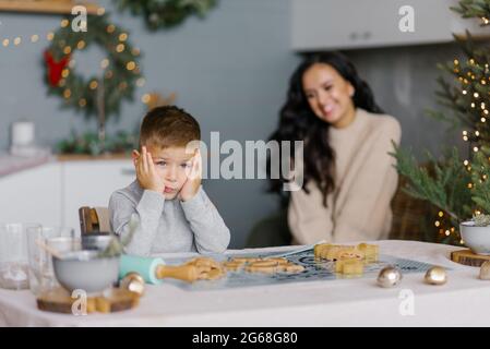 Mamma e figlio fanno i volti e si divertono a preparare i biscotti di Natale in cucina Foto Stock