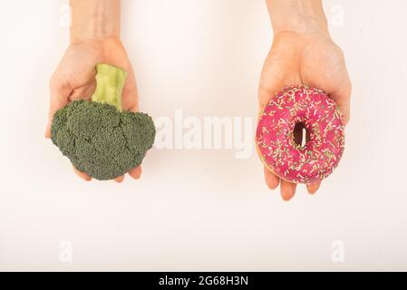 Confronto delle abitudini alimentari. Donna che tiene broccoli e ciambella su sfondo bianco Foto Stock