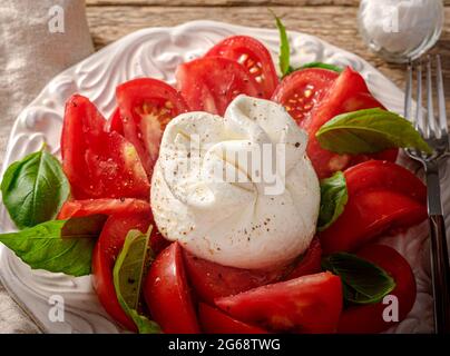 Insalata burrata su piatto bianco vintage. Vista dall'alto dell'insalata con burrata e foglie di basilico. Foto Stock