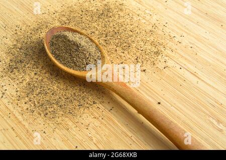 Macinato di pepe nero in polvere fresco e aromatico, in cucchiaio su tagliere di bambù in legno Foto Stock