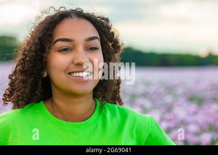 Razza mista bella African American biracial ragazza adolescente femmina giovane donna che indossa t shirt verde nel campo di fiori rosa o viola papaveri al mq Foto Stock