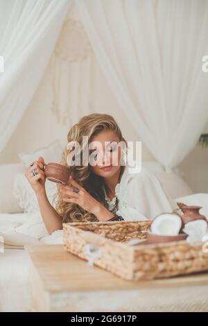 Bella donna bionda ama bere caffè e cocco. Donna che si rilassa in un hotel tropicale Foto Stock