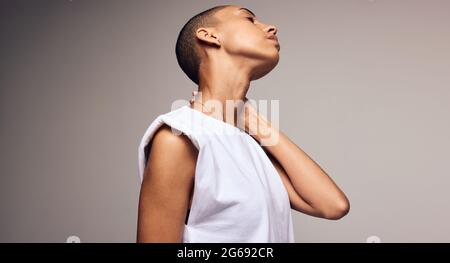 Femmina androgino con testa rasata in piedi su sfondo colorato. Donna con la mano sul collo e gli occhi chiusi. Foto Stock