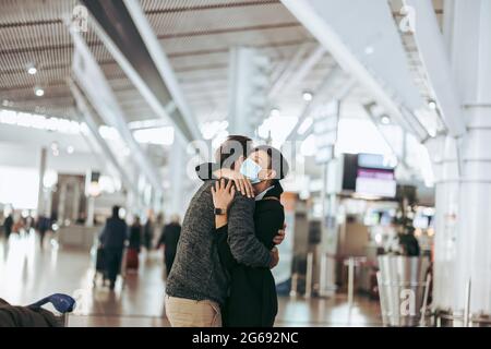 viaggiatore che abbraccia la donna al cancello di arrivo dell'aeroporto. Donna in maschera di saluto uomo dopo l'arrivo dal tour post pandemia. Foto Stock