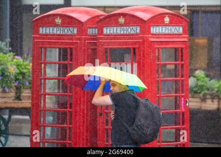 Un uomo si rifugia sotto un ombrello durante una discesa di pioggia a Covent Garden, Londra, come parti del Regno Unito sono colpiti da pioggia pesante e temporali. Data immagine: Domenica 4 luglio 2021. Foto Stock