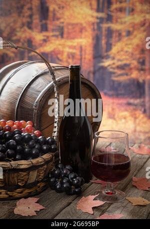 Bicchiere di vino rosso e uva fresca all'aperto su un rustico tavolo in legno con sfondo autunnale Foto Stock