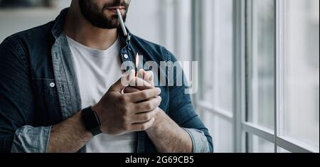 Frustrato giovane uomo stressato che fuma sigaretta, abitudini malsane e dipendenza dal tabacco Foto Stock