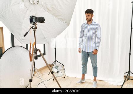 Giovane arabo che si pone come modello in studio di fotografia scettico e nervoso, accigliato sconvolto a causa del problema. Persona negativa. Foto Stock