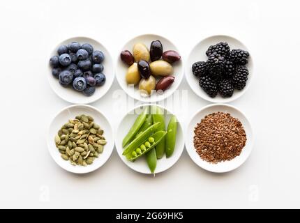 Vista dall'alto di un piccolo piatto di vari ingredienti sani, tra cui semi, verdure, olive e bacche. Foto Stock