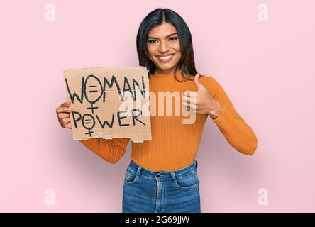 Giovane latino transessuale transgender donna che tiene la bandiera di potere della donna sorridente felice e positivo, pollice in su facendo eccellente e segno di approvazione Foto Stock