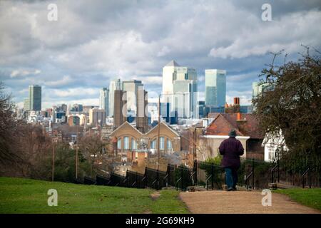 Uomo che cammina attraverso Greenwich Park con vista su Canary Wharf e la centrale elettrica di Greenwich sullo sfondo - Londra. Foto Stock