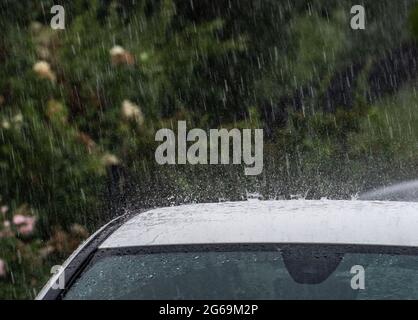 04 luglio 2021, Hessen, Francoforte sul meno: Pioggia pesante cade sul tetto di un'auto nel quartiere di Bornheim. Il Servizio meteorologico tedesco (DWD) aveva messo in guardia da forti tempeste in alcune parti dell'Assia. Foto: Frank Rumpenhorst/dpa Foto Stock