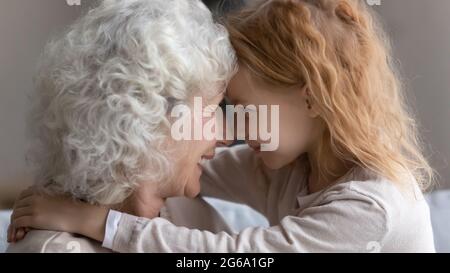 Sorridente nipotina ragazza abbraccio collo di nonna matura ritirata Foto Stock