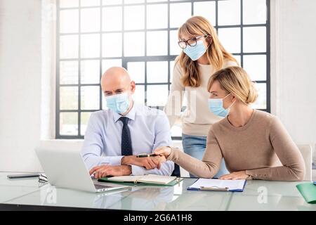 Gruppo di uomini d'affari che indossano maschere per il viso mentre lavorano insieme in ufficio. Lavoro di squadra. Foto Stock