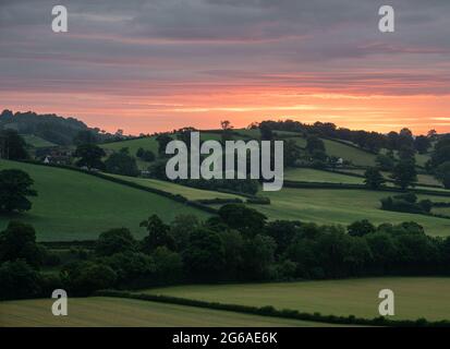 Campi verdi in un paesaggio rurale con un'alba arancione brillante Foto Stock