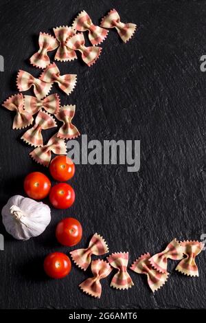Pasta farfalle, pomodori e aglio su ardesia nera Foto Stock