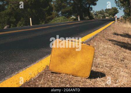 Primo piano di una valigia di colore giallo vintage vicino alla strada del paese. Foto Stock