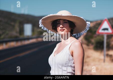 Ritratto di una donna di 20 anni con un cappello di paglia hitchhiking presso la strada del paese Foto Stock