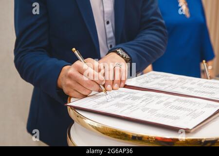 Le mani dell'uomo dello sposo hanno messo sulla firma nella rivista circa il consenso al matrimonio al matrimonio. Foto Stock