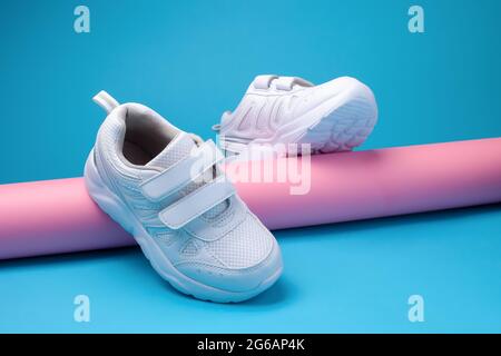 immagine promozionale di un equilibrio di due scarpe da running girly bianche su un tubo di carta lungo rosa su sfondo blu Foto Stock