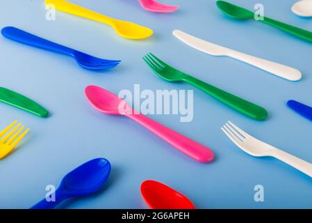 Il motivo delle posate riutilizzabili su sfondo blu. Cucchiai, forcelle, coltelli in plastica. Picnic estivo. Concetto di riciclo della plastica Foto Stock